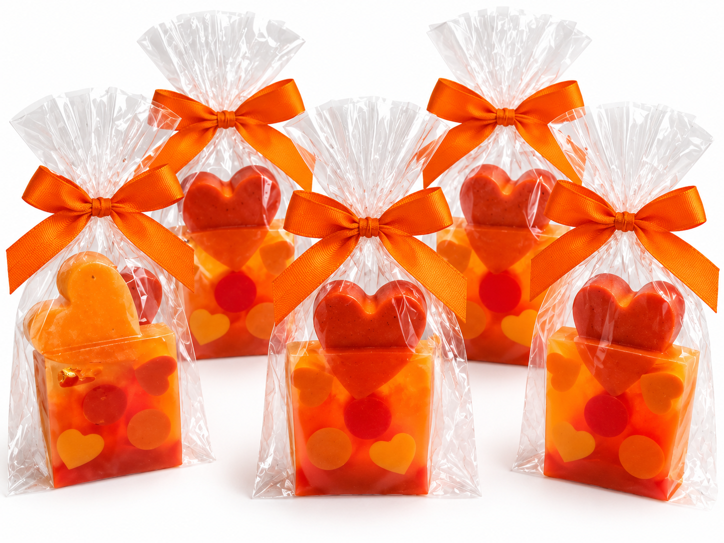 Heart-shaped goat milk soap favors in clear cellophane bags tied with bright orange satin bows